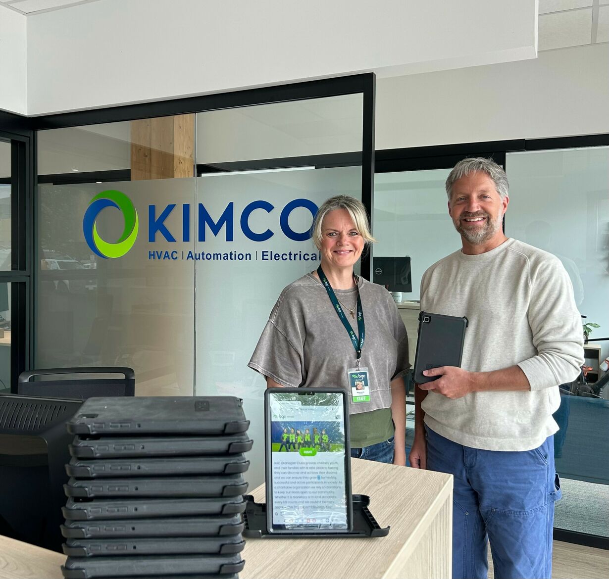 Two Kimco Controls technicians in high-visibility jackets and hard hats carry tools and rope across a commercial rooftop HVAC installation, wrapping up work at end of day.