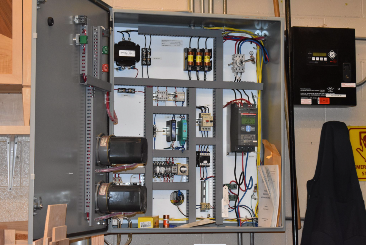 An open electrical control panel with neatly routed wiring, fuses, relays and a motor controller display, beside a spark detection system controller.