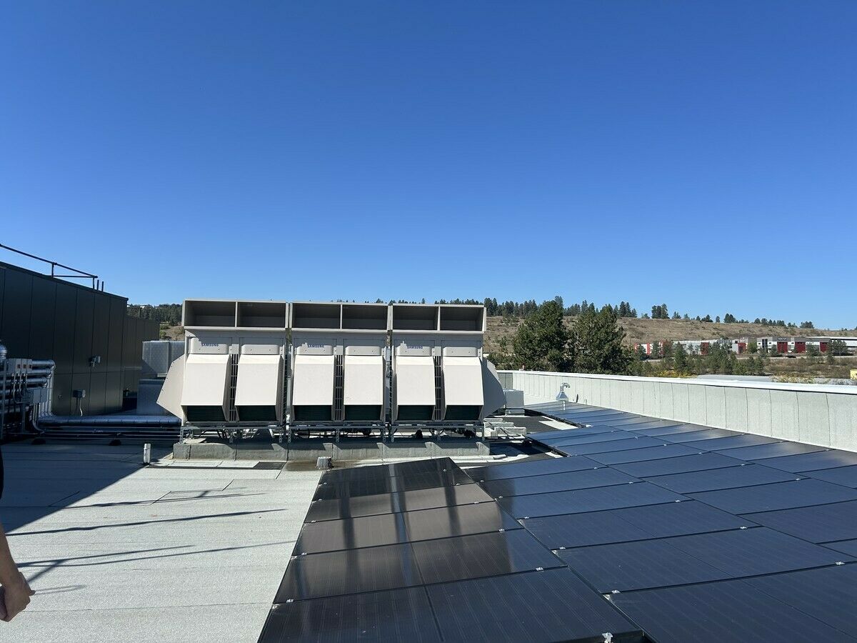 Rooftop energy recovery ventilator units beside solar panels, with hills and trees visible in the background.